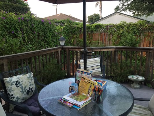 A patio table with books and art supplies surrounded by greenery