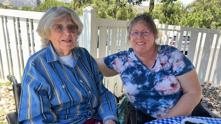 An elderly resident and staff member outside, enjoying a sunny day