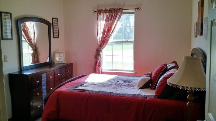 A well-decorated bedroom featuring a bed with red and white bedding, a wooden dresser, and a lamp.