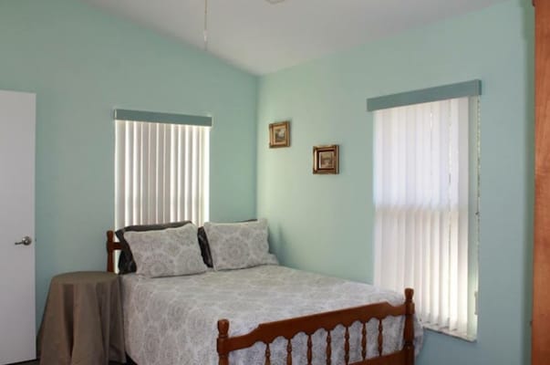 A cozy bedroom with a bed, light blue walls, and natural light from windows.
