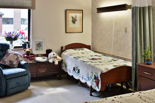 A cozy bedroom featuring a bed with a floral quilt, armchair, and decorative items.