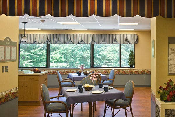 Dining area with tables set for a meal, featuring floral decorations and large windows