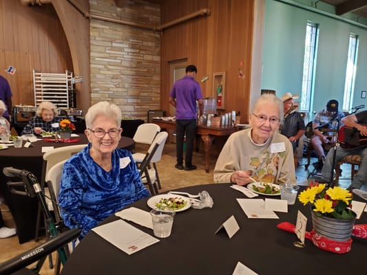 Two smiling senior women enjoying lunch at a community event