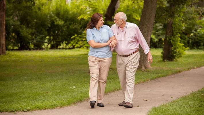 Caregiver and resident walking together in a garden setting