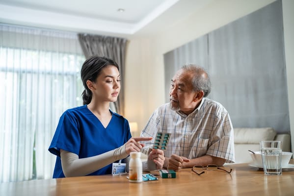A caregiver discusses medication with a senior man at a table.