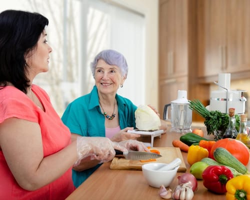 Two women cooking together in a kitchen filled with fresh vegetables.