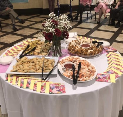 A beautifully arranged table of food with residents in the background