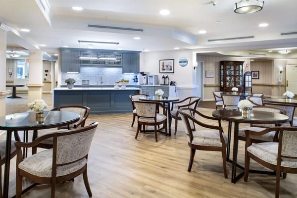 Cozy common area featuring tables and chairs with a kitchen backdrop.