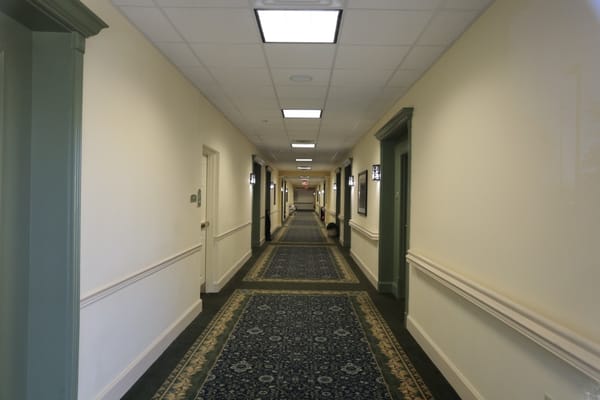Long, well-lit hallway with decorative carpet and doors to residents' rooms.