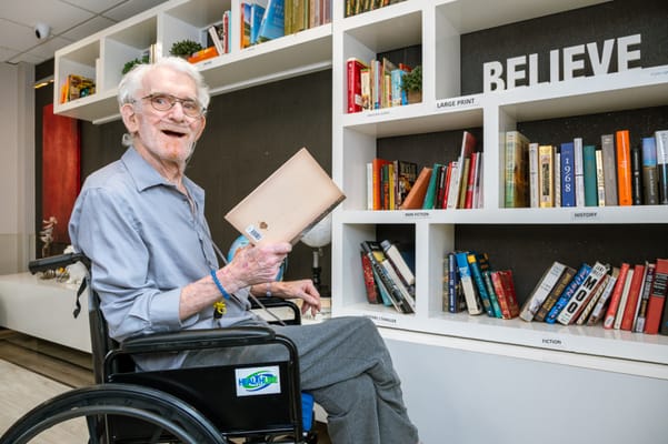 A resident in a wheelchair enjoying a book in the library