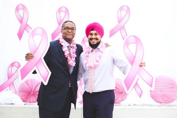 Two men wearing leis and holding large pink ribbons