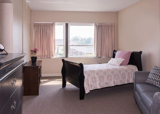 Well-lit private resident room with bed and furniture