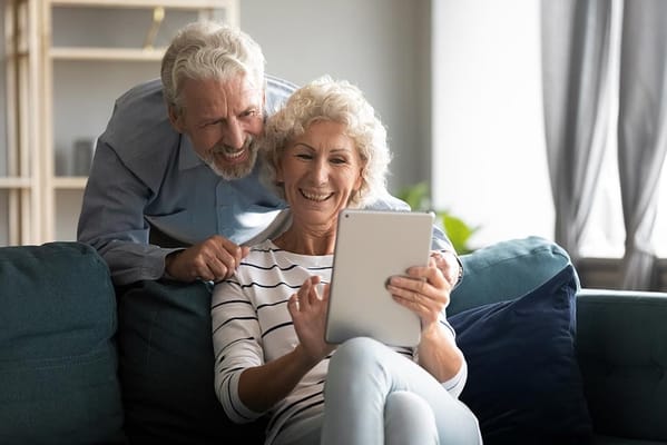 Two seniors smiling while using a tablet together
