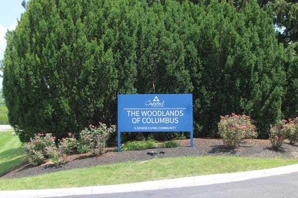 Sign for The Woodlands of Columbus by landscaped entrance