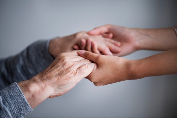 Hands of an elderly person and a caregiver clasping each other
