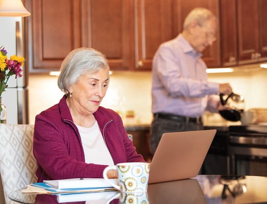 A senior woman working on a laptop in a kitchen setting