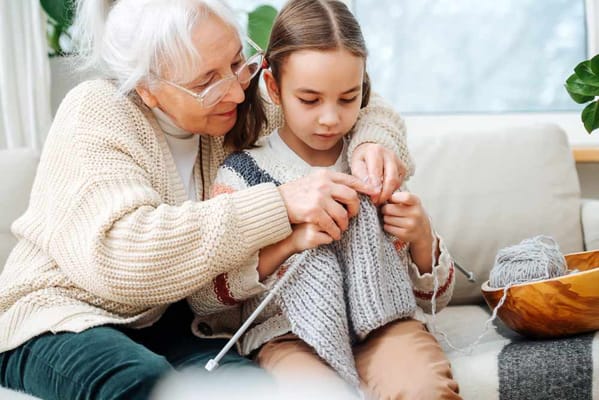 An elderly woman knitting with a young girl