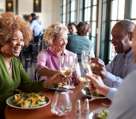 Four residents enjoying a meal and toasting in the dining room