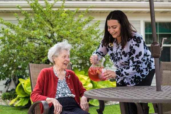 Caregiver serving a drink to a resident outdoors