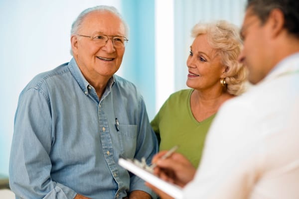 Elderly man smiling with two caregivers in a bright room