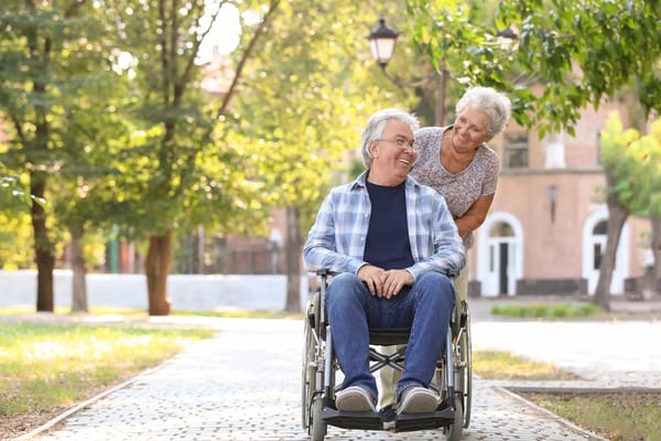 A senior man in a wheelchair smiling with a caregiver in a garden