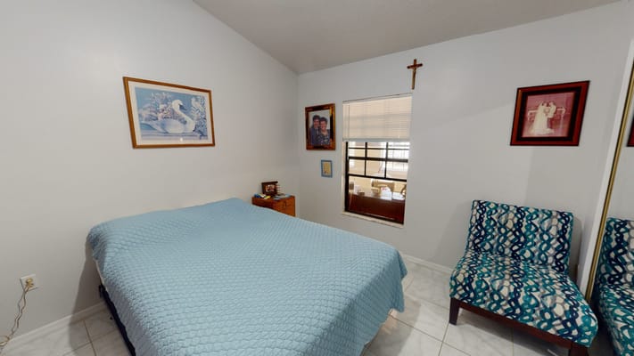 A cozy bedroom with a blue quilt, framed photos, and a chair