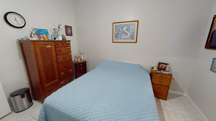A neatly arranged bedroom with a blue quilt, wooden dresser, and framed pictures.