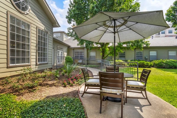 Outdoor patio with seating under an umbrella surrounded by greenery