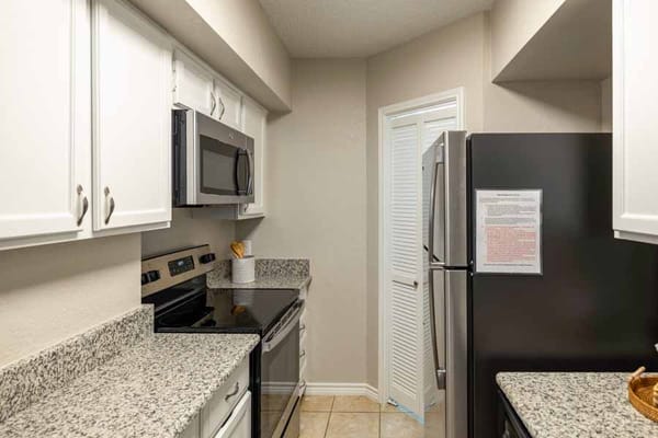 Compact kitchen featuring granite countertops, stainless steel appliances, and white cabinets.