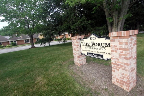 Sign for The Forum at the Crossing featuring brick pillars and greenery.