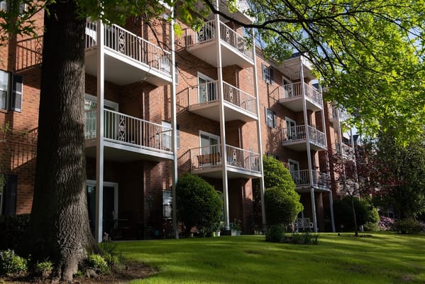 Brick building with balconies surrounded by green lawn and trees