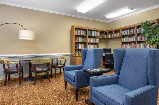A library area featuring blue armchairs, a reading table, and bookshelves filled with books.
