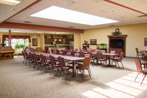 Spacious common area with tables and chairs, and a piano in the corner.