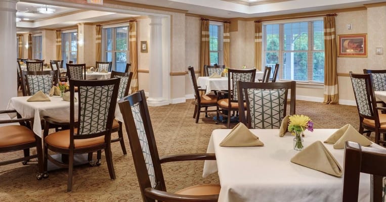 A dining area with elegantly set tables and chairs in a senior living facility.