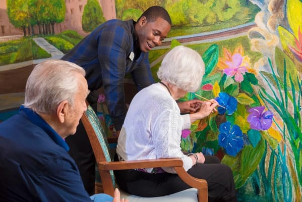 Senior residents participating in an art activity with staff in front of a colorful mural.