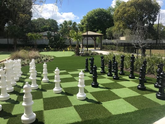 Large outdoor chess set with white and black pieces on green artificial turf.