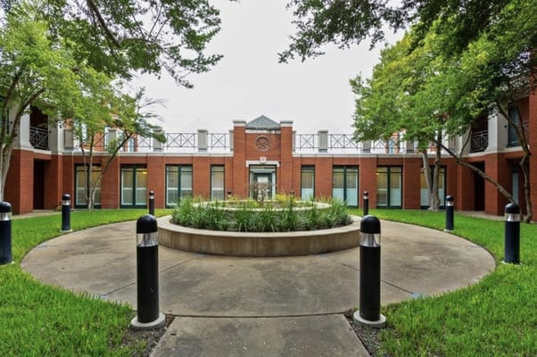 A serene courtyard featuring a circular garden surrounded by green grass and trees.