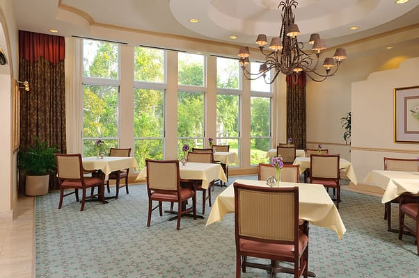 Bright dining area with tables and chairs, large windows, and a chandelier.