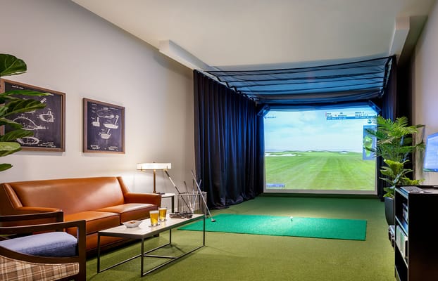 A cozy indoor golf simulator setup with a couch and drinks.