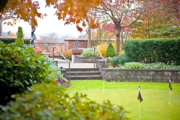 A garden path leading to a cozy seating area surrounded by greenery and seasonal foliage.