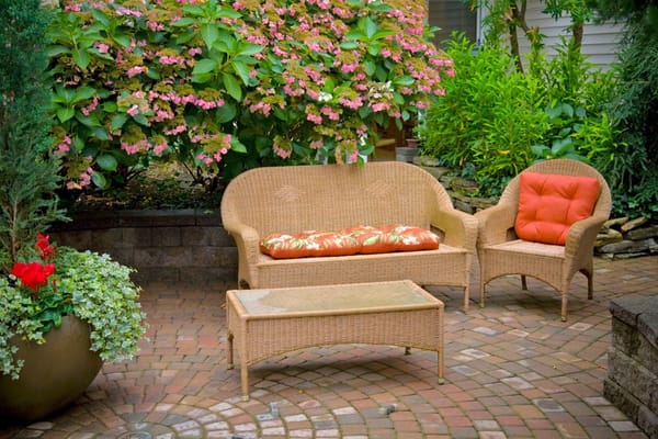 Wicker sofa and chair with floral cushions in a landscaped garden
