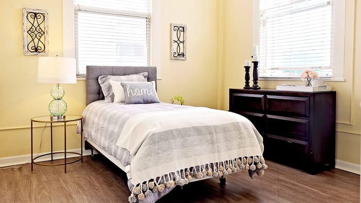 A neatly arranged bedroom featuring a single bed with decorative pillows and a bedside lamp.