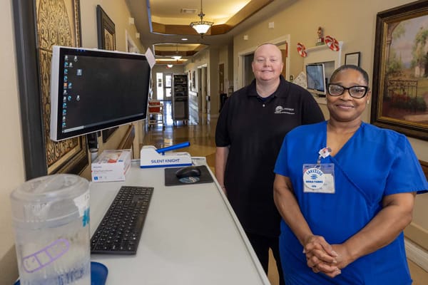 Two staff members standing in a hallway with a computer.