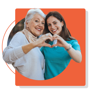 A resident and caregiver smiling and making a heart shape