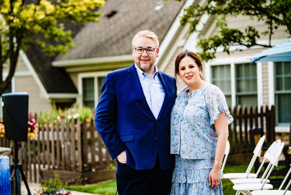 Two people smiling outdoors near the facility building