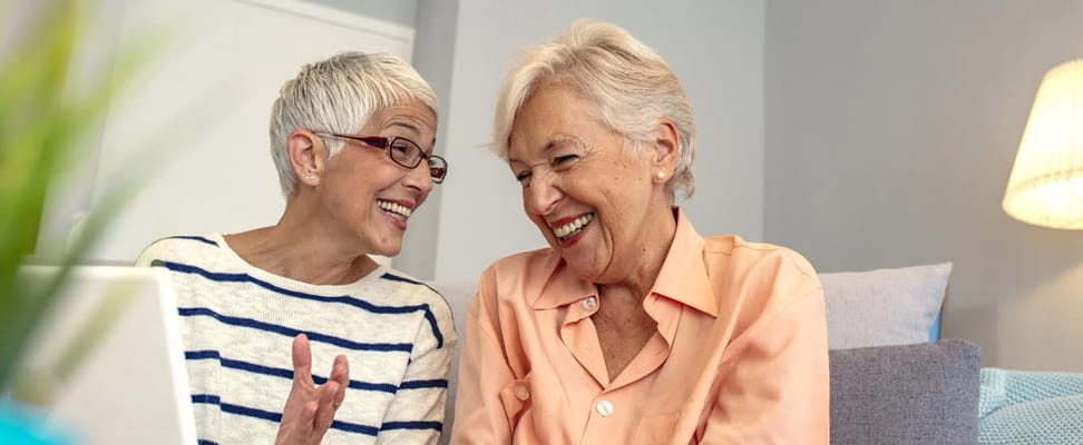 Two senior women laughing together in a cozy indoor setting