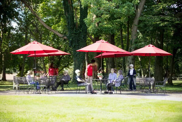 Residents enjoying a sunny outdoor gathering under red umbrellas.