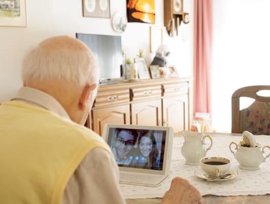 An elderly man using a tablet to video chat with family in a cozy interior.