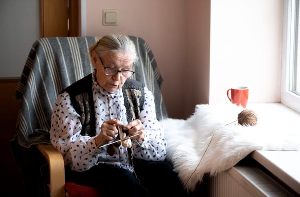 Elderly woman knitting by a sunny window
