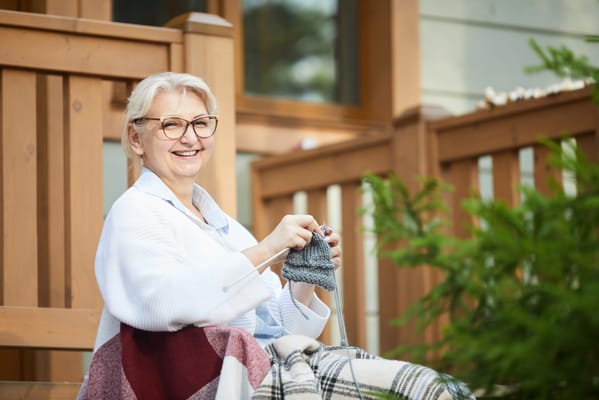 A resident knitting on a porch with greenery
